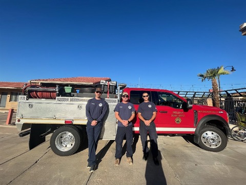 Three firefighters stand next to a red truck.